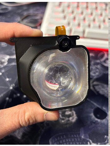 A lens and its printed carrier held up to the light.